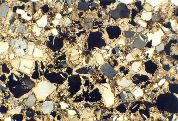 A thin film slice of rock shows grains packed closely together, displaying low porosity